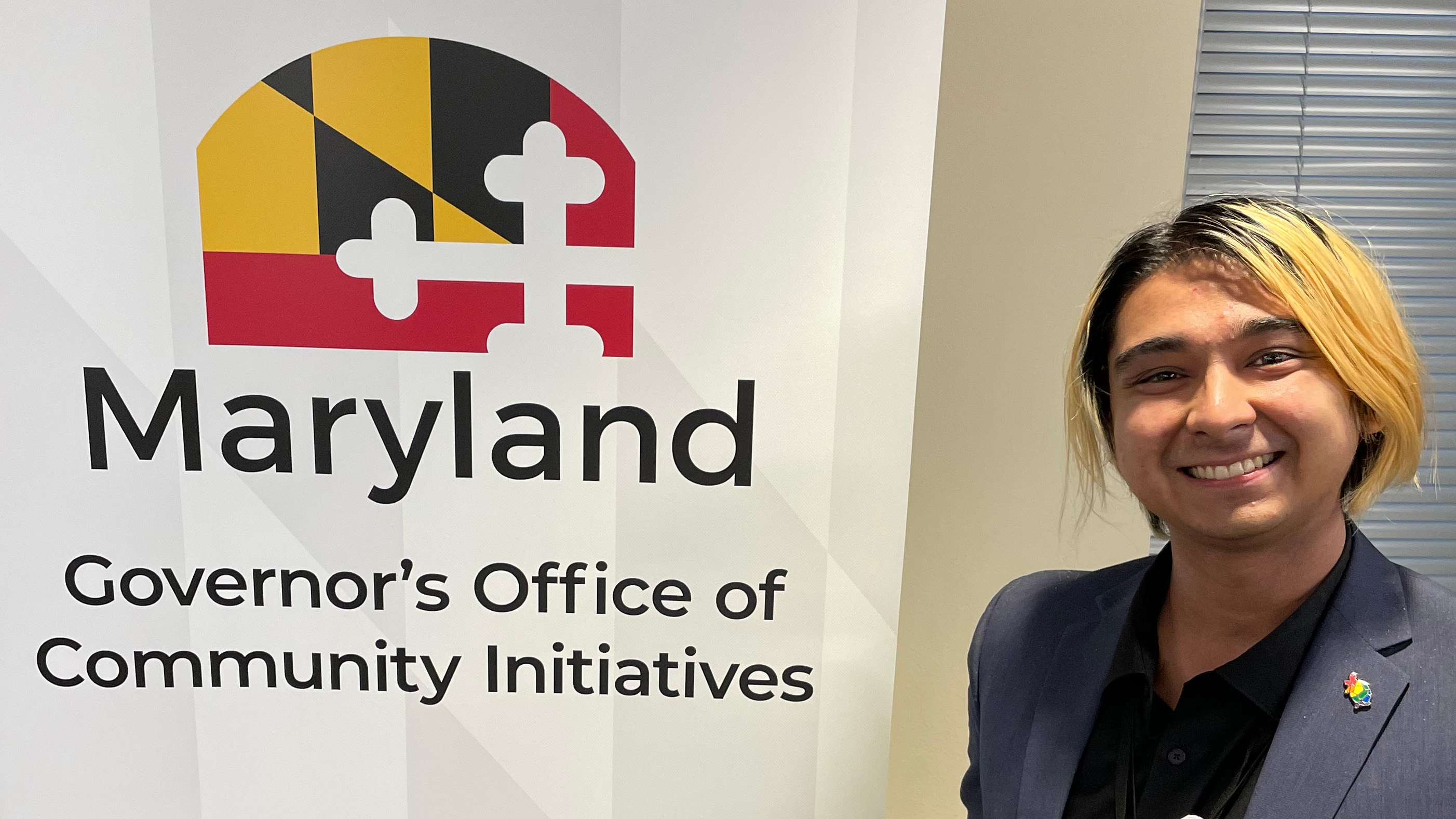 Photo of M Pease next to Maryland Governor's Office of Community Initiatives sign